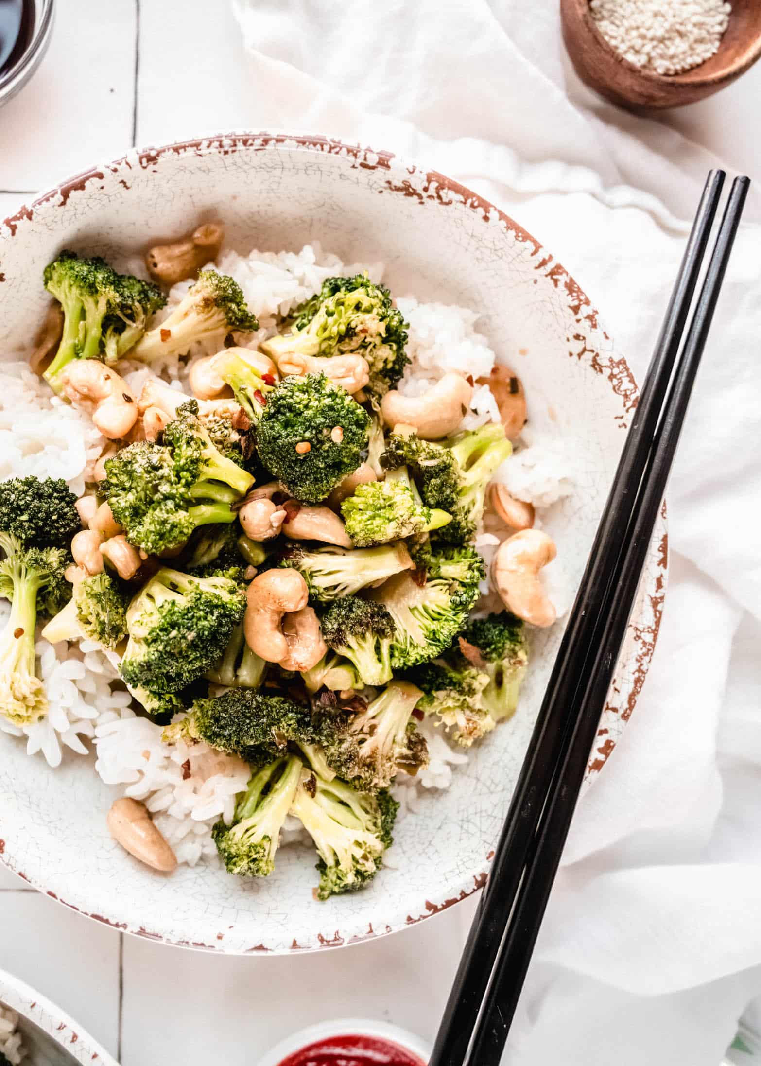 Broccoli cashew stir fry served over fluffy white rice in a rustic bowl, featuring crisp-tender broccoli florets, toasted cashews, and a glossy savory sauce, styled with chopsticks on the side.