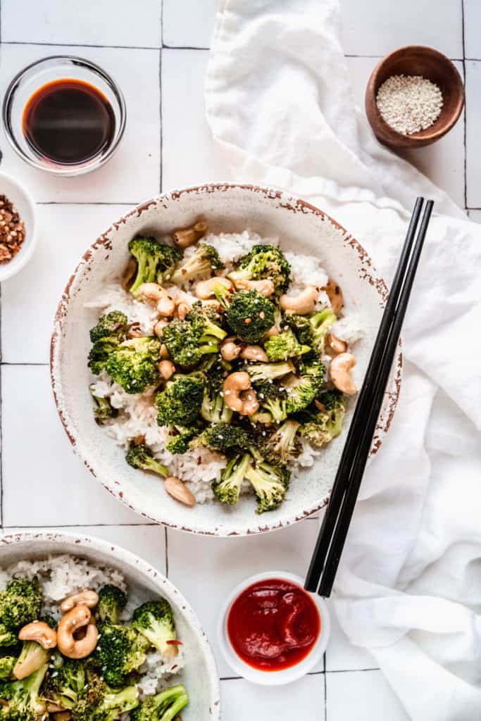 broccoli cashew stir fry in a bowl over white rice with chopsticks placed on top of bowl.  