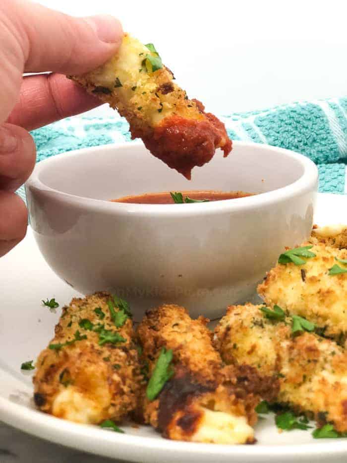 mozzarella sticks on plate, hand dipping one in marinara sauce