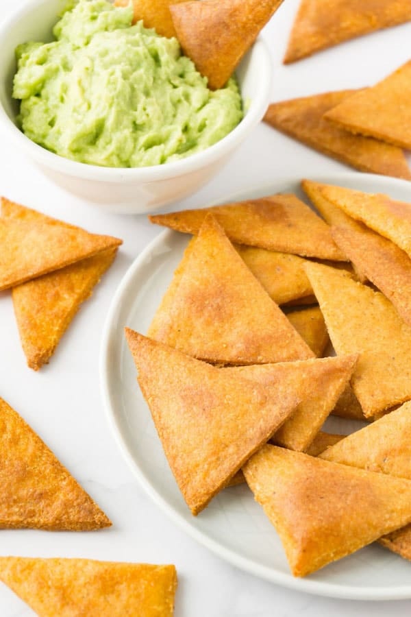 homemade tortilla chips on plate next to bowl of guacamole 