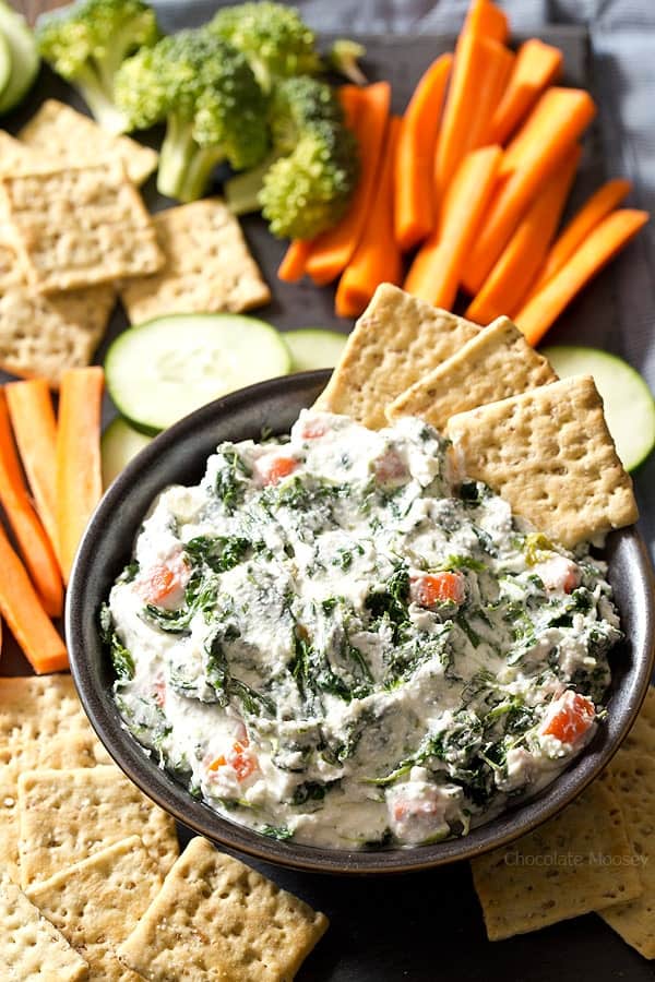 creamy spinach dip in bowl with crackers and veggies on platter
