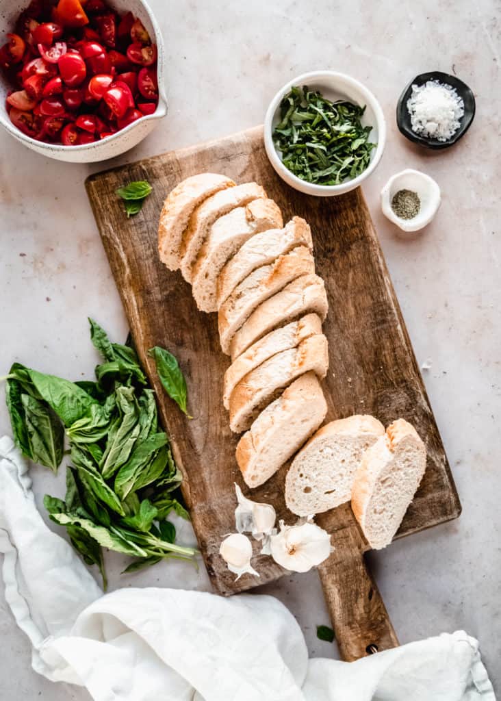 sliced baguette on wood cutting board with basil chiffonade in bowl 