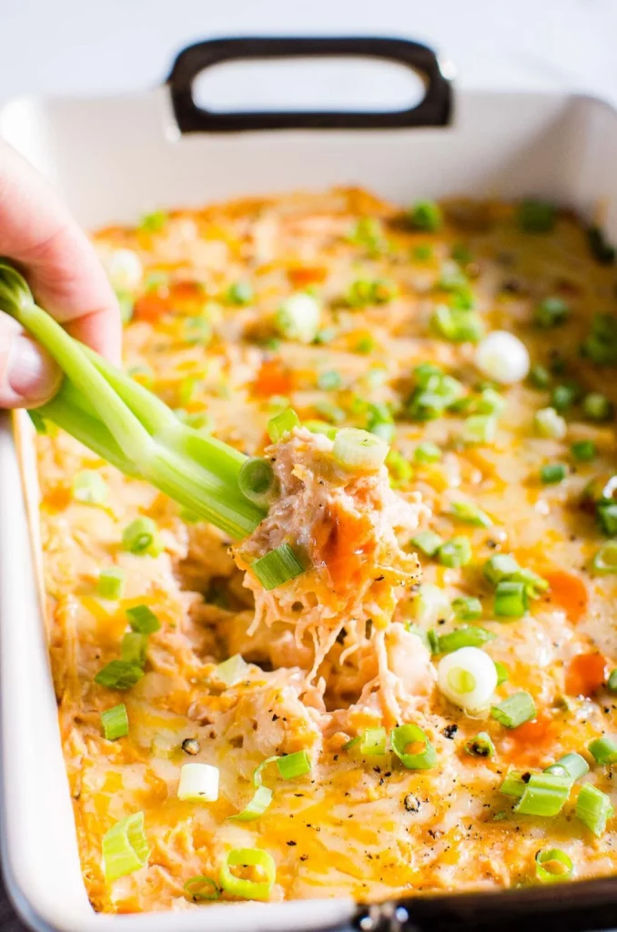 buffalo chicken dip in baking dish being scooped out with celery stick 