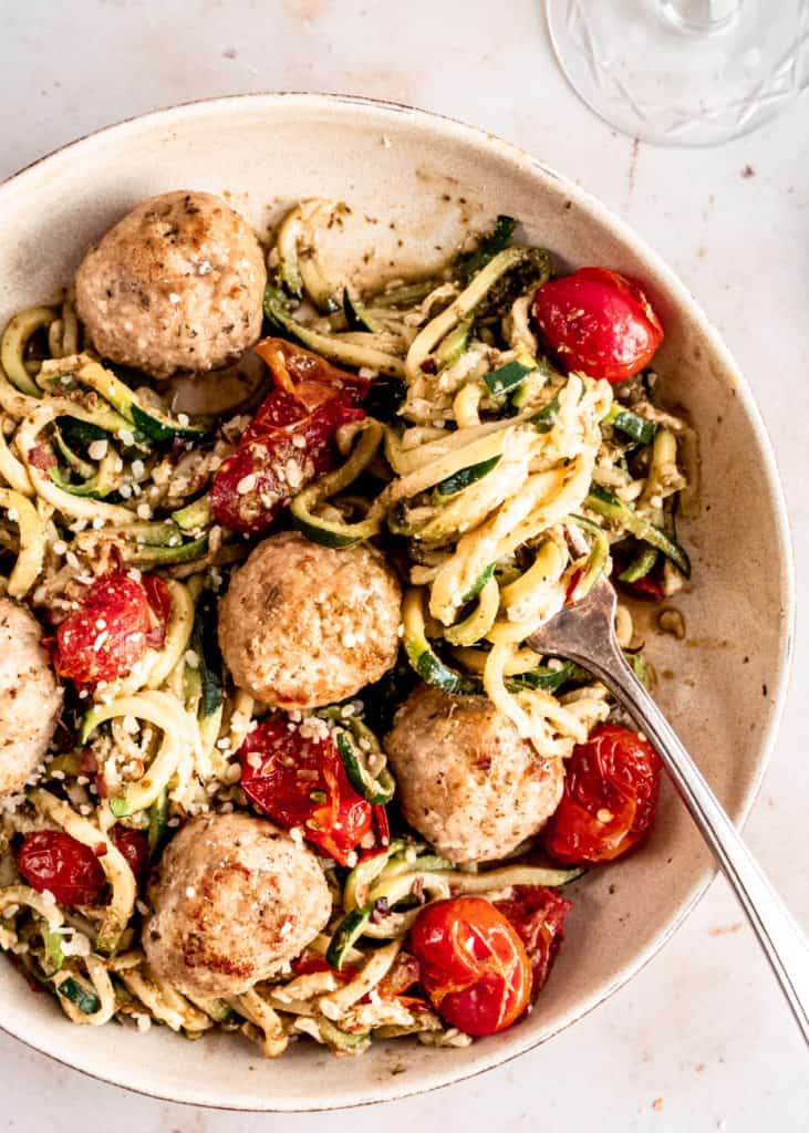 Pesto zucchini noodles twirled around fork in bowl with meatballs 