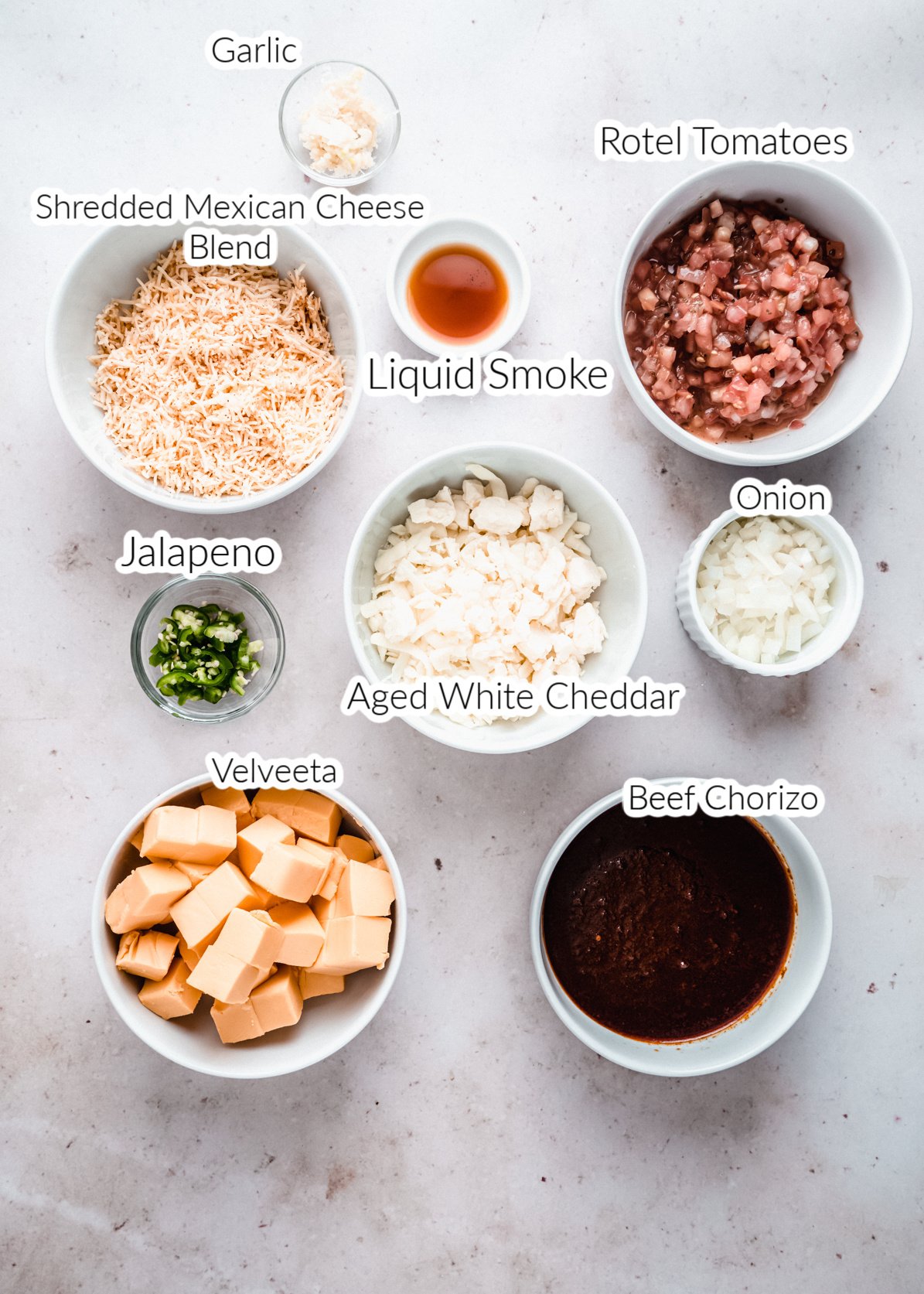 smoked queso dip ingredients in individual bowls on a white background 
