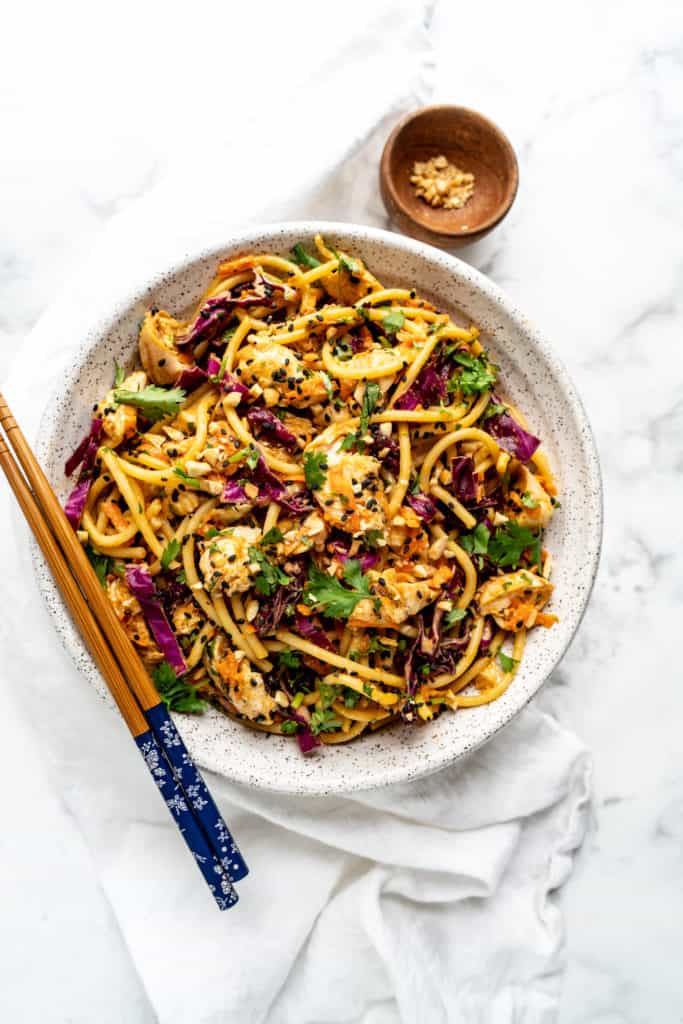 spicy peanut noodles garnished with cilantro in large bowl with chopsticks 