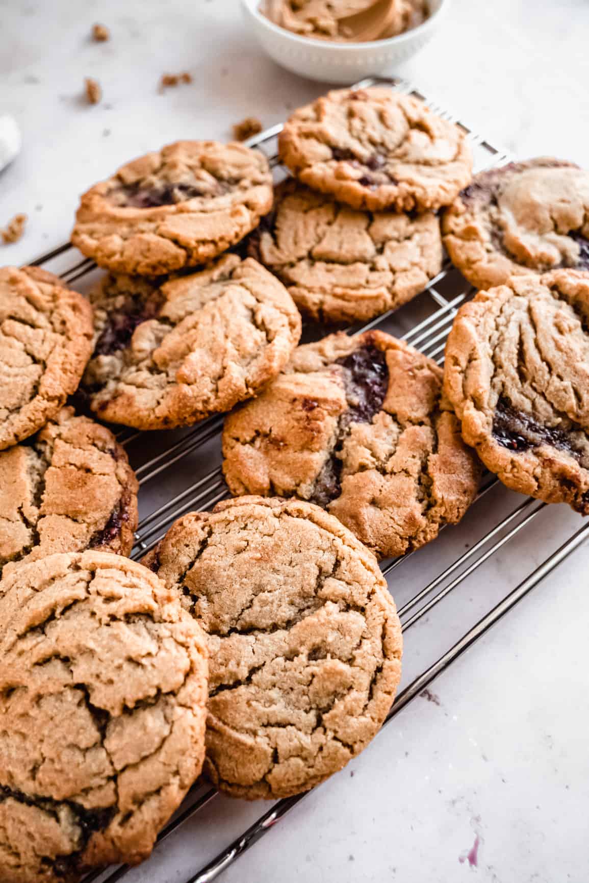 a close up shot of a batch of peanut butter and jelly cookies cooling on a wire rack, with crackly golden-brown tops and swirls of dark jelly peeking through the soft, chewy centers.