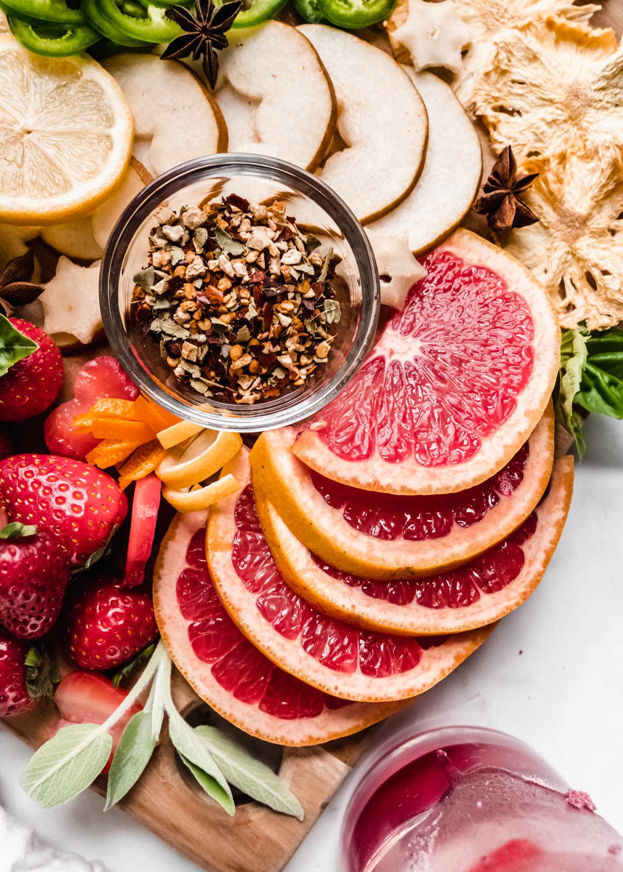 close up of sliced fresh grapefruit, strawberries, sliced grapefruit on cocktail garnish board 