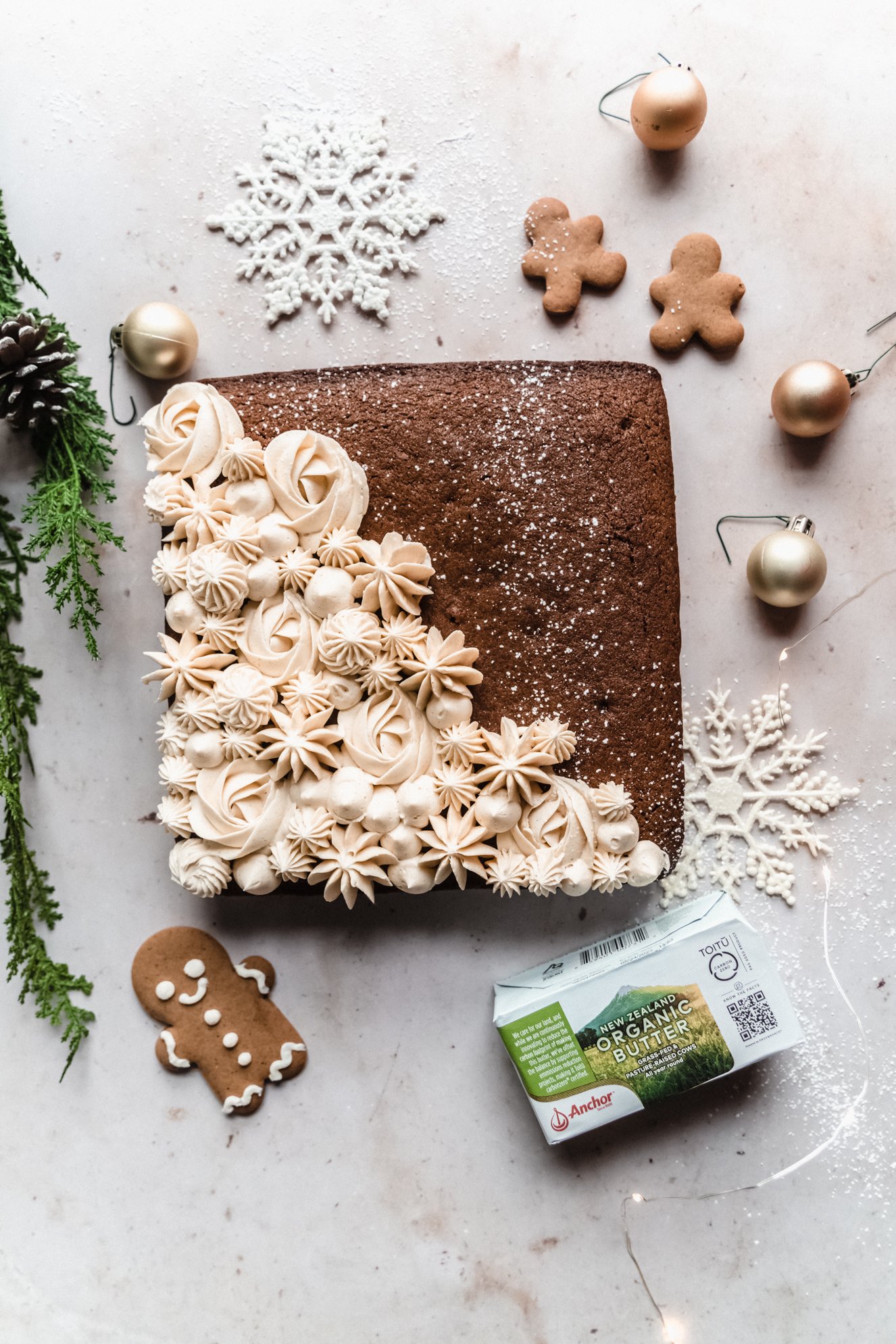 gingerbread snack cake frosted on marble backdrop with twinkle lights and greenery surrounded by gingerbread men 