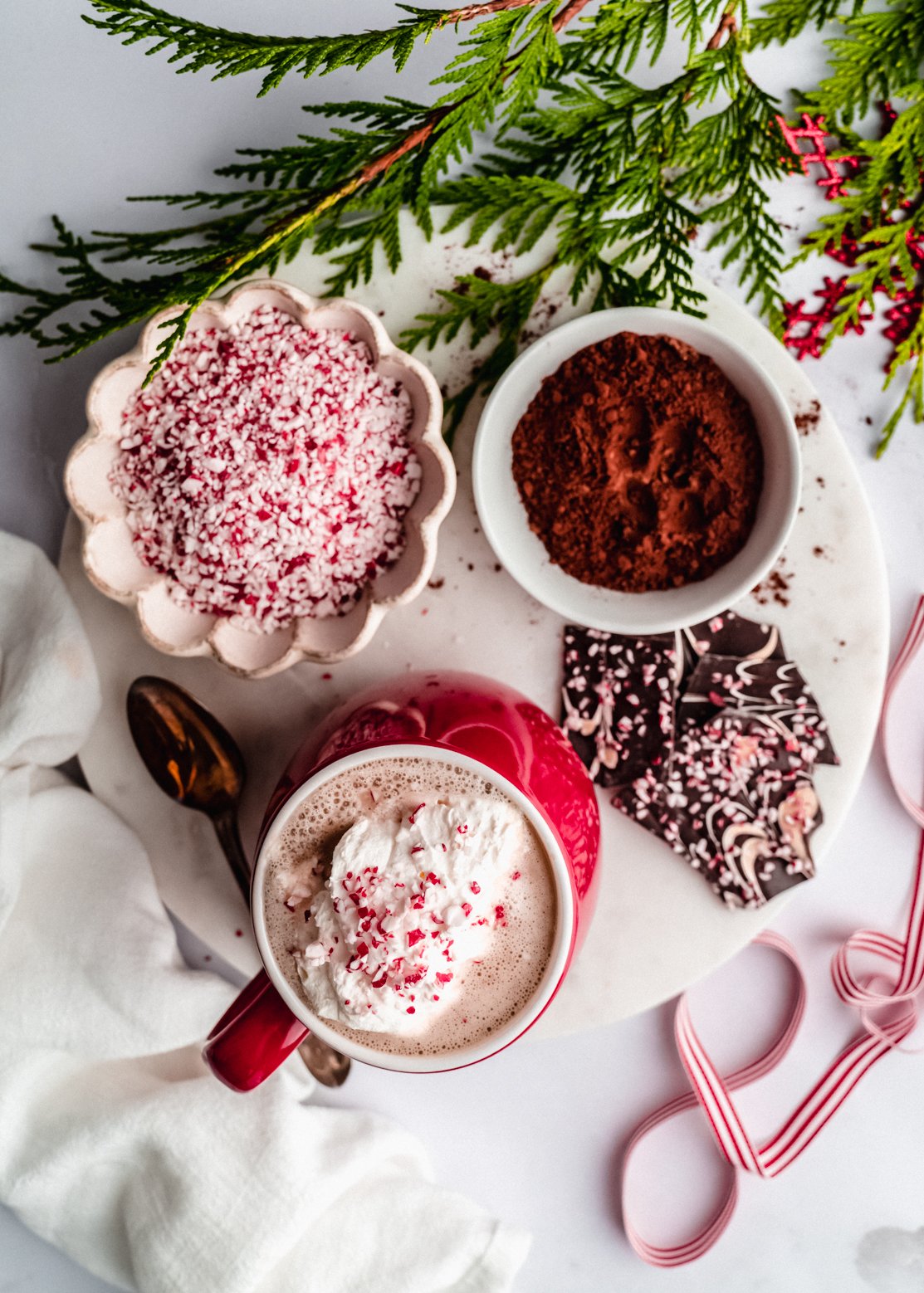 overhead shot of peppermint latte on marble platter with peppermint pieces in bowl and peppermint bark on platter 