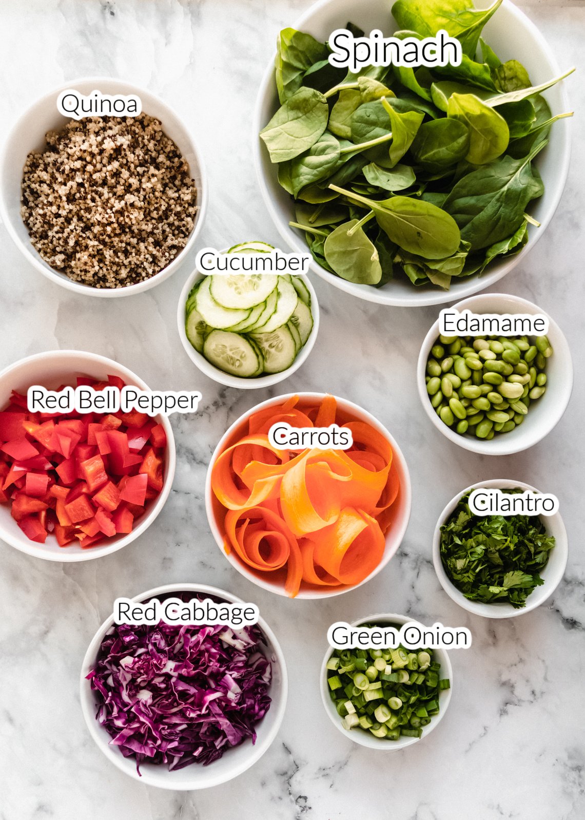 ingredients for asian edamame salad in individual bowls on marble backdrop