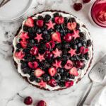 fruit pizza topped with cherries, watermelon, blueberries and blackberries on marble surface and pie serving utensil laying to the right