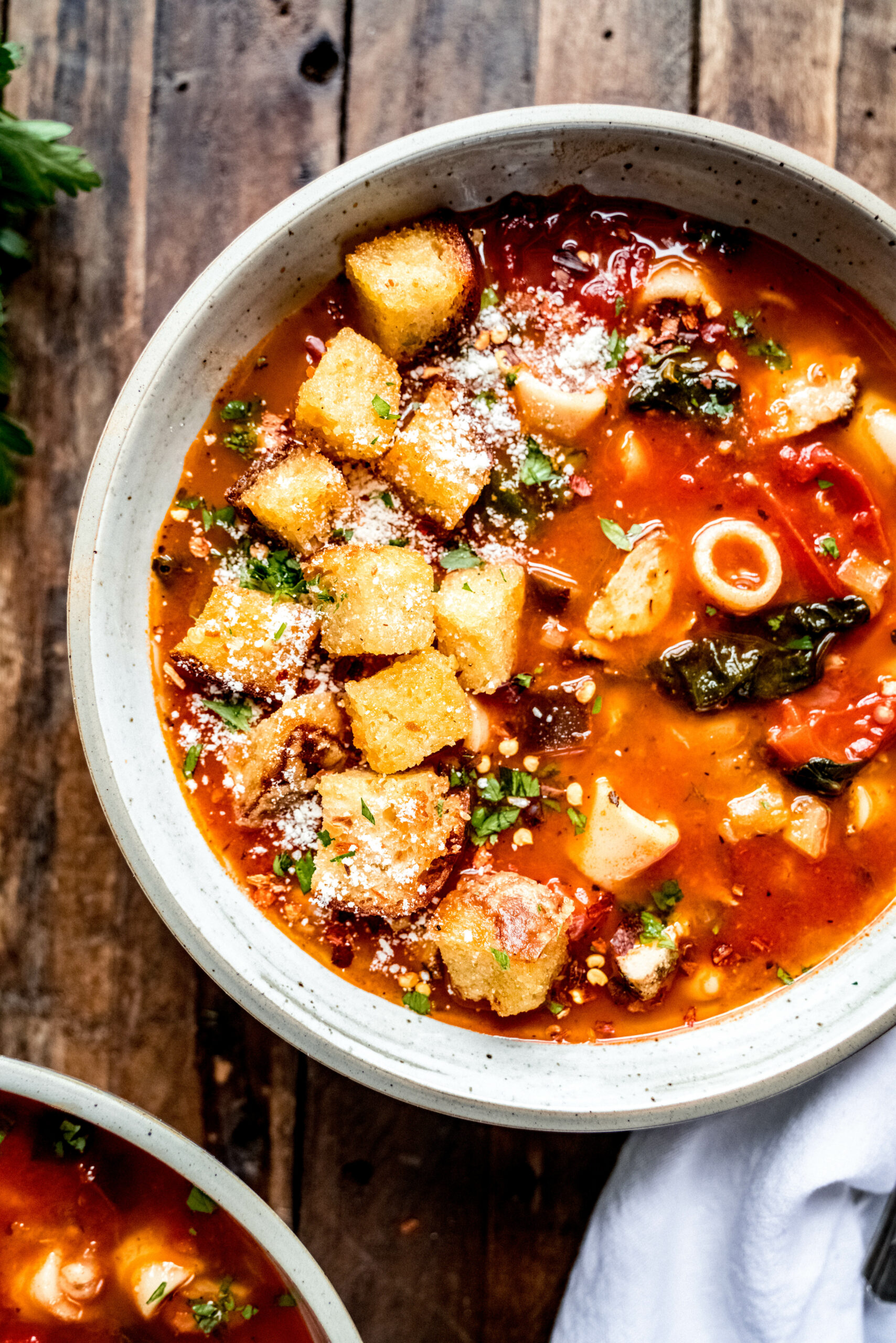 Overhead shot of of instant pot minestrone soup garnished with fresh herbs, grated parmesan and croutons with a white napkin next to the bowl laying on a wood surface 