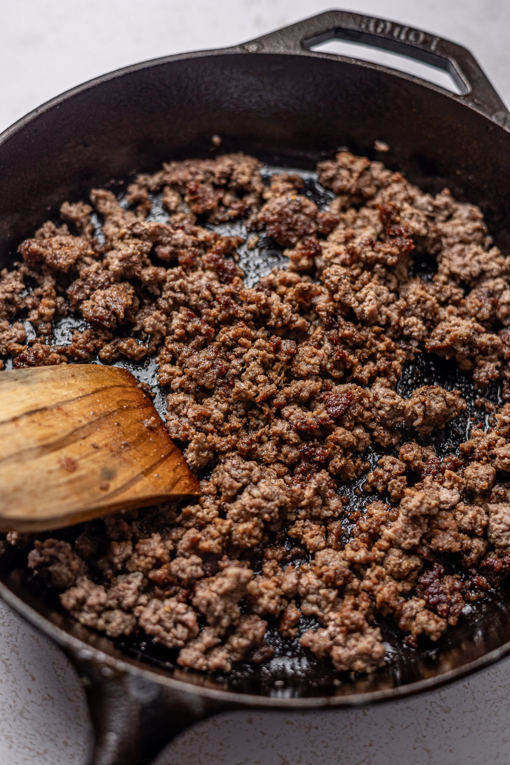 side by side of raw then cooked ground beef in cast iron skillet for burger bowl 