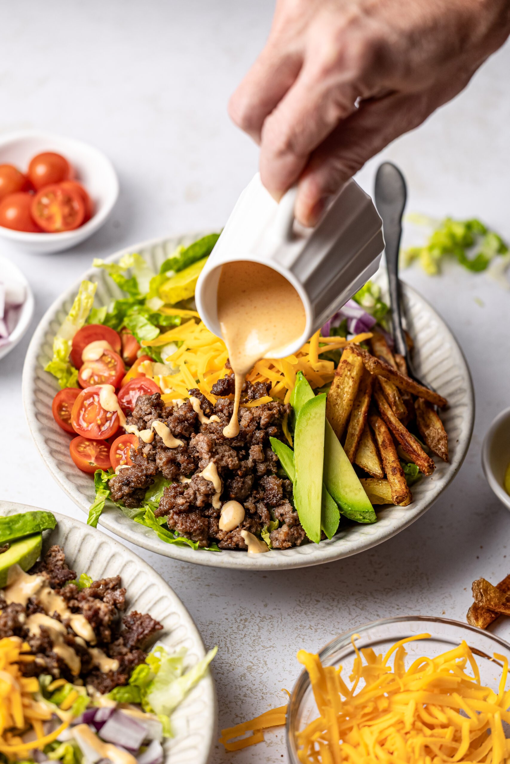 completed burger bowl in bowl with vessel of special sauce being poured over bowl 