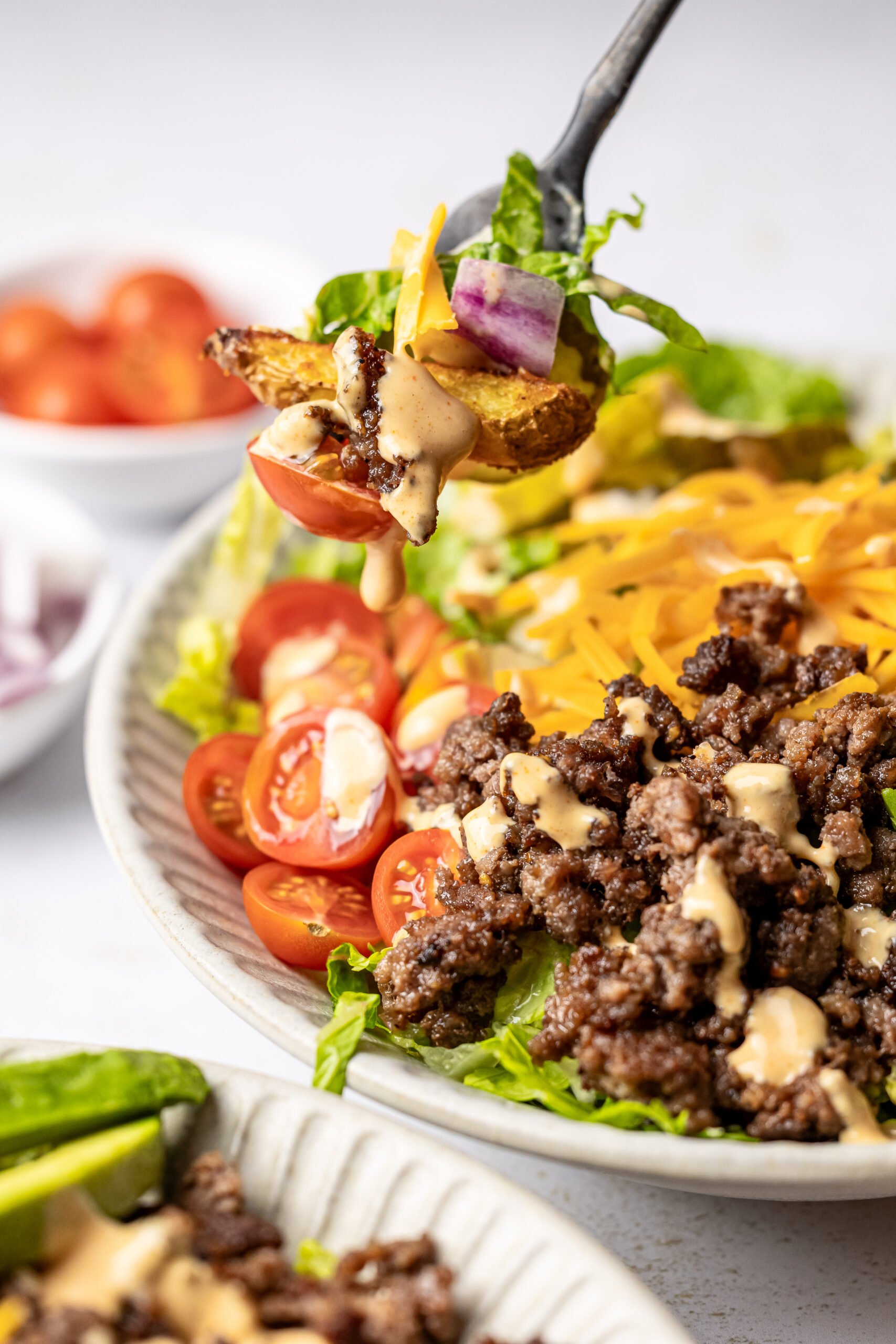 a fork full of burger bowl ingredients in front of burger bowl drizzled with special sauce 