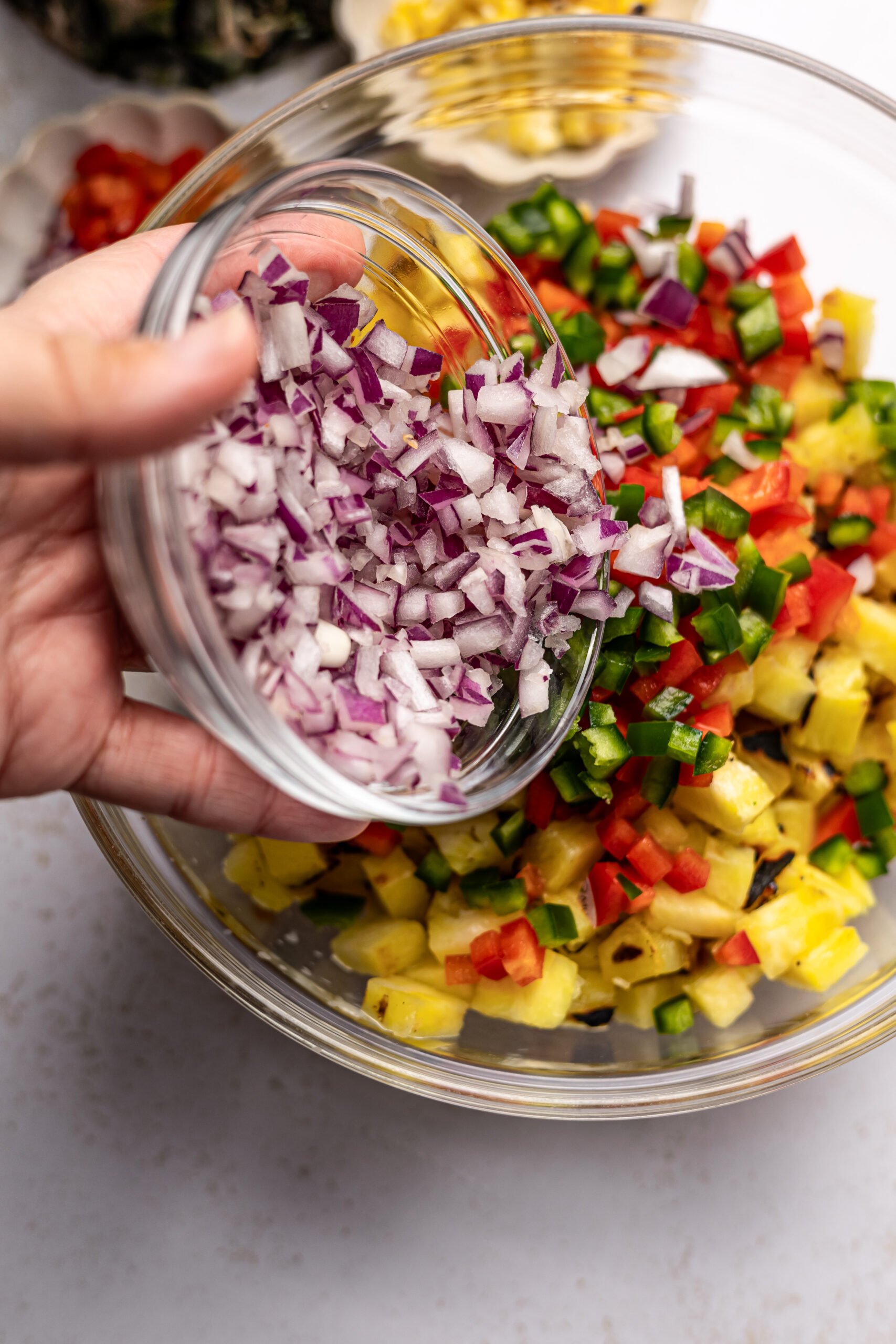 chopped red onion being poured into glass bowl with other Corn and pineapple salsa ingredients 