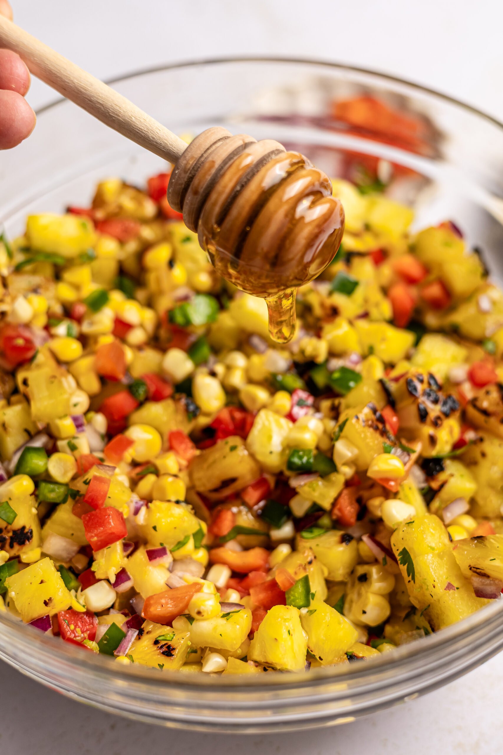  Corn and Pineapple Salsa in a glass bowl being drizzled with honey with a dipper 