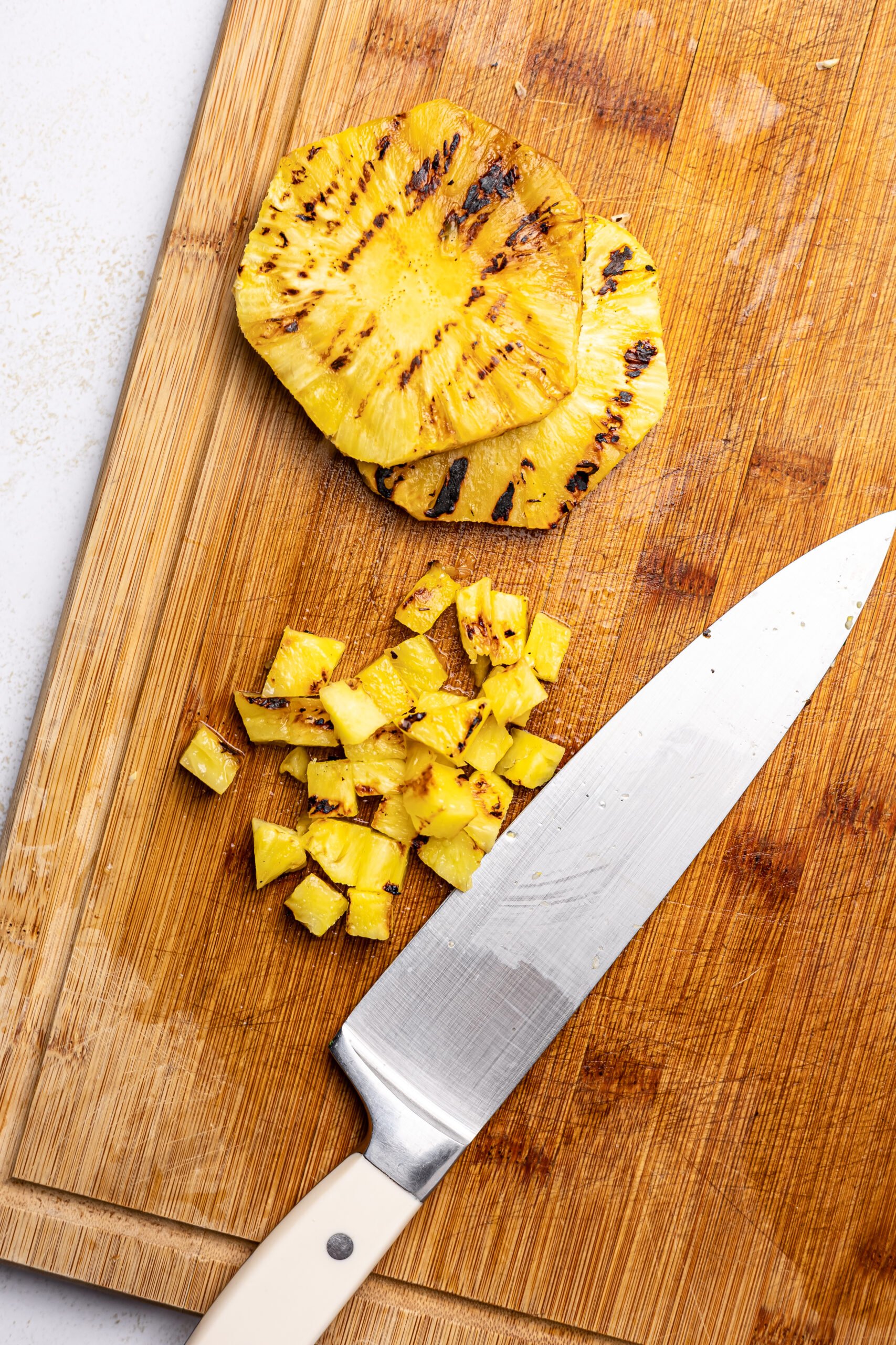 grilled pineapple for Corn and pineapple salsa on a cutting board with a chefs knife next to it 