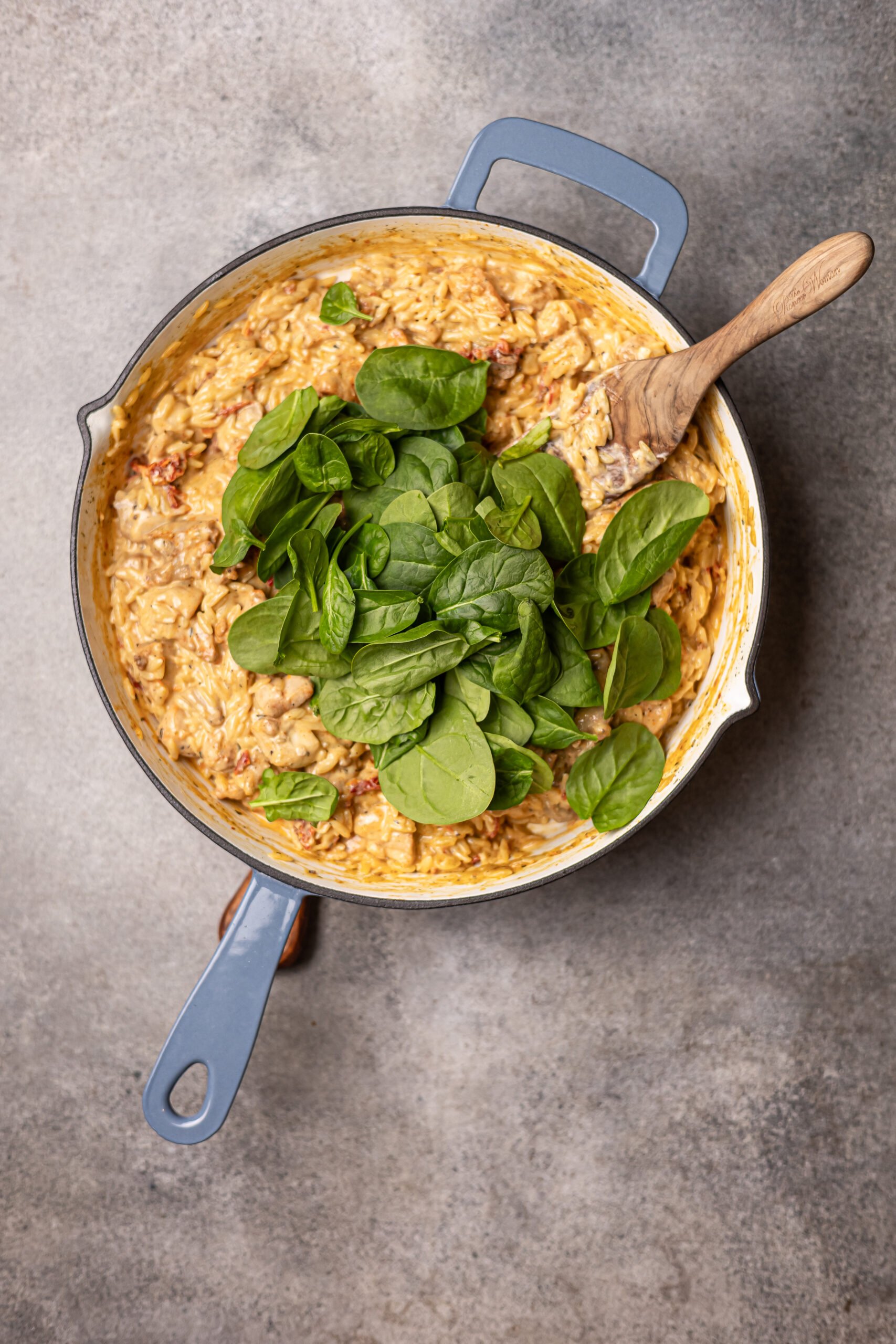marry me chicken orzo in grey skillet, fresh spinach is on top.  There's a wooden spoon in the skillet 