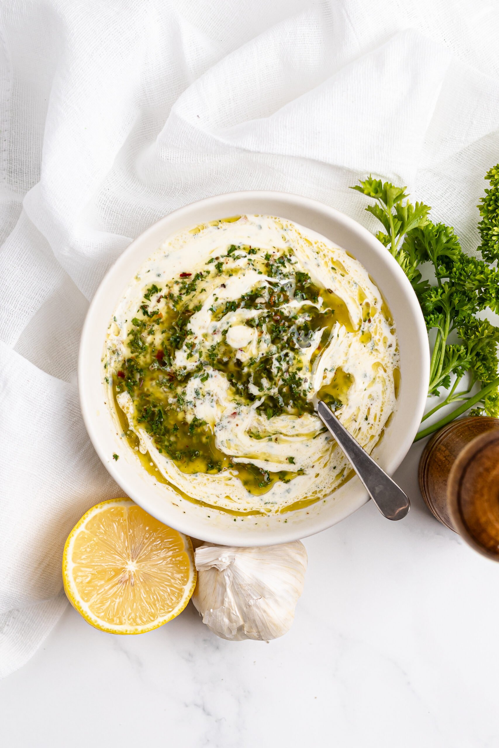 overhead shot of chimichurri aioli in a small bowl surrounded by a lemon wedge and fresh parsley