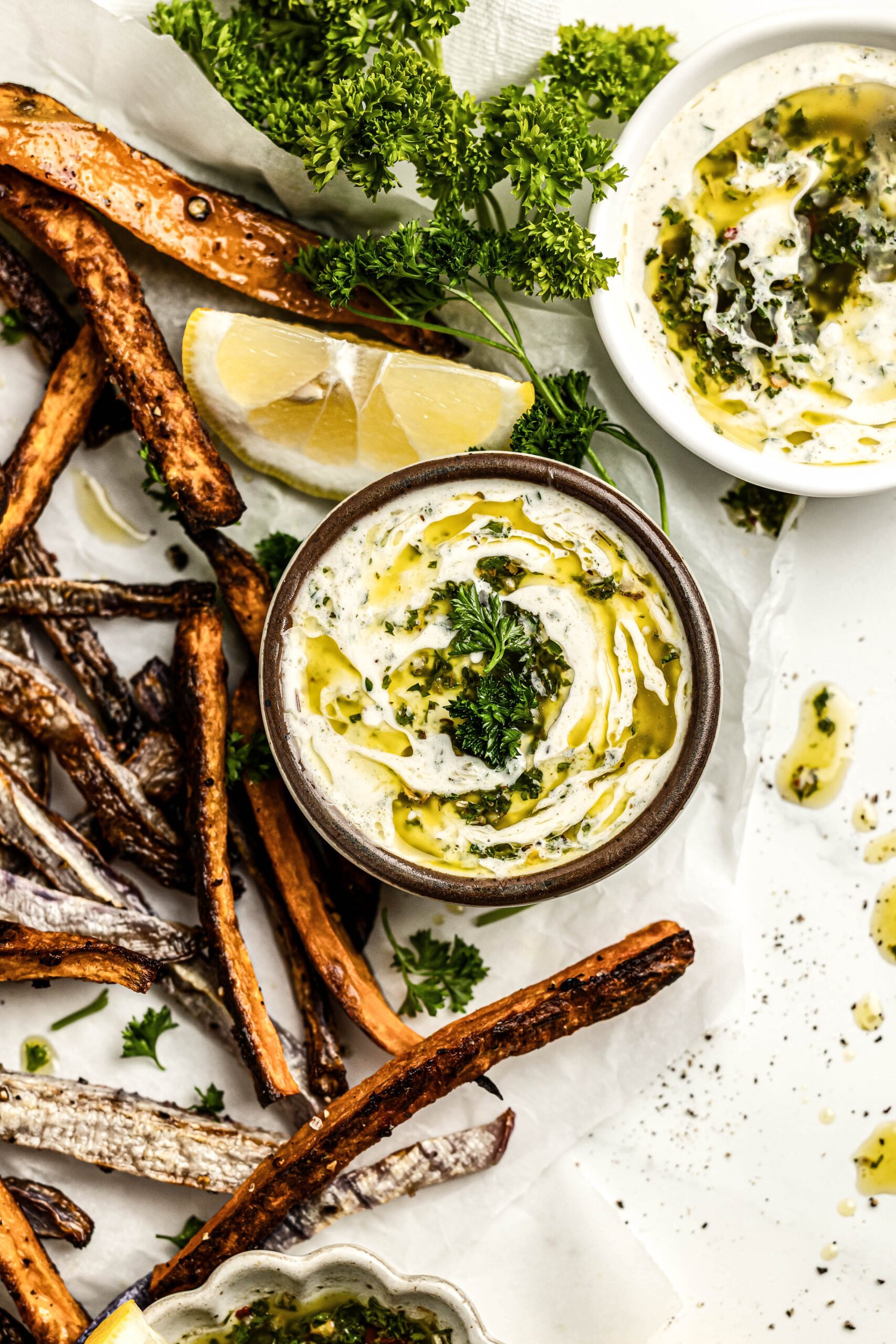 chimichurri aioli in a small bowl surrounded by crispy french fries, a lemon wedge and fresh parsley