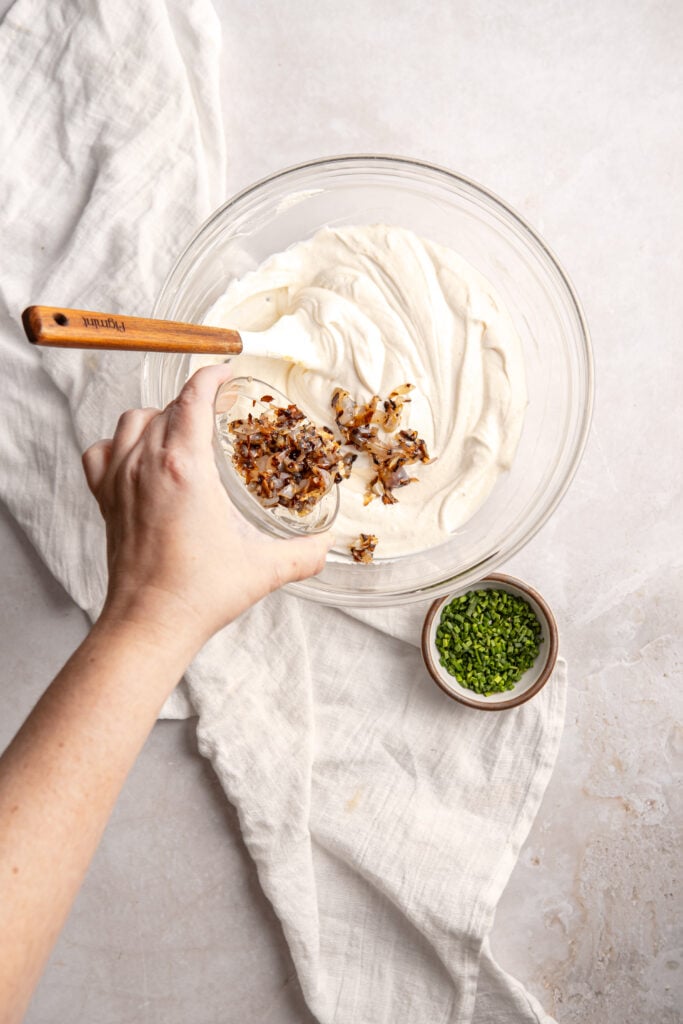 pouring carmelized onions into the sour cream base for the homemade sour cream and onion dip 