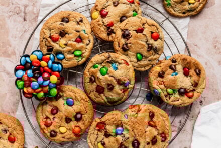 Cooling rack filled with freshly baked chewy M&M cookies loaded with colorful candy pieces and chocolate chips, with a small bowl of M&Ms placed alongside.