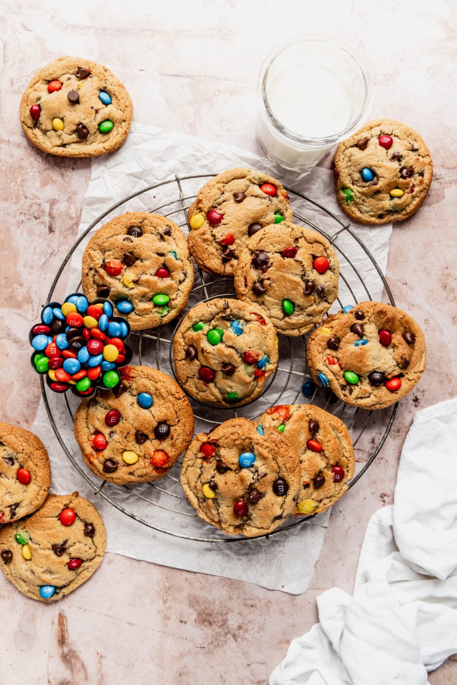 Cooling rack filled with freshly baked chewy M&M cookies loaded with colorful candy pieces and chocolate chips, with a small bowl of M&Ms placed alongside.