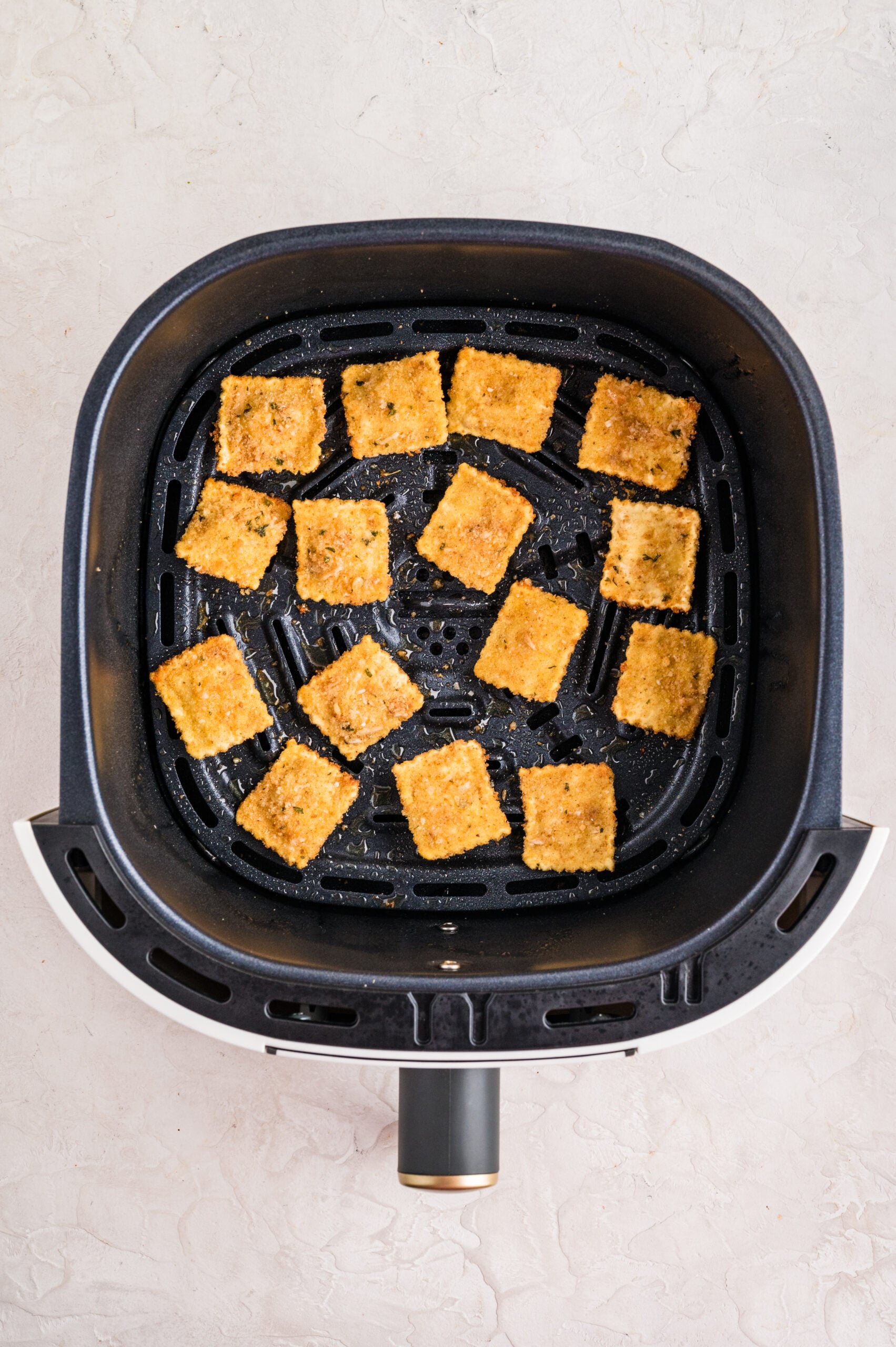 Crispy breaded air fryer toasted ravioli arranged in a single layer inside the air fryer basket after cooking, showing their golden brown texture.