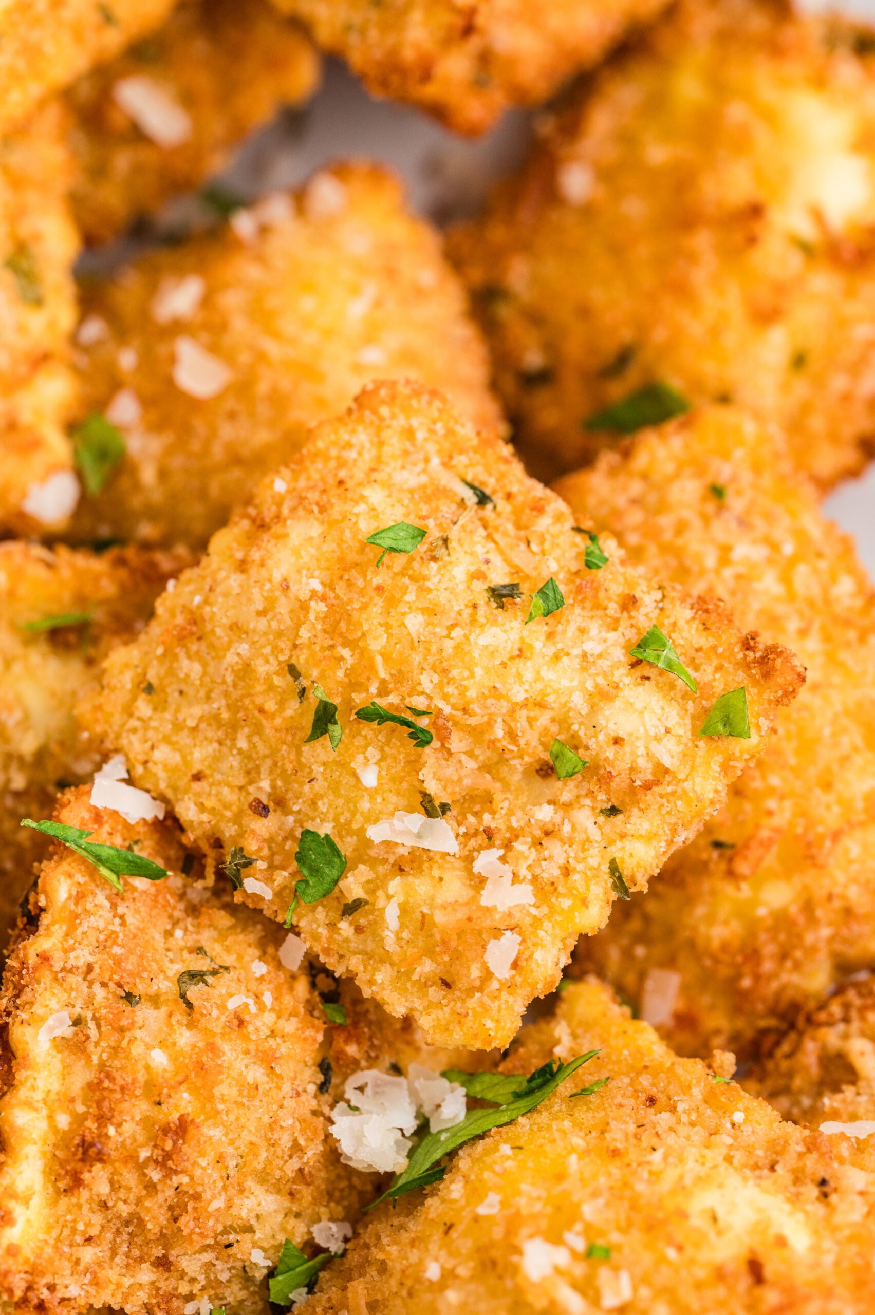 Close-up of crispy air fryer toasted ravioli coated in golden breadcrumbs and sprinkled with parmesan and fresh parsley.