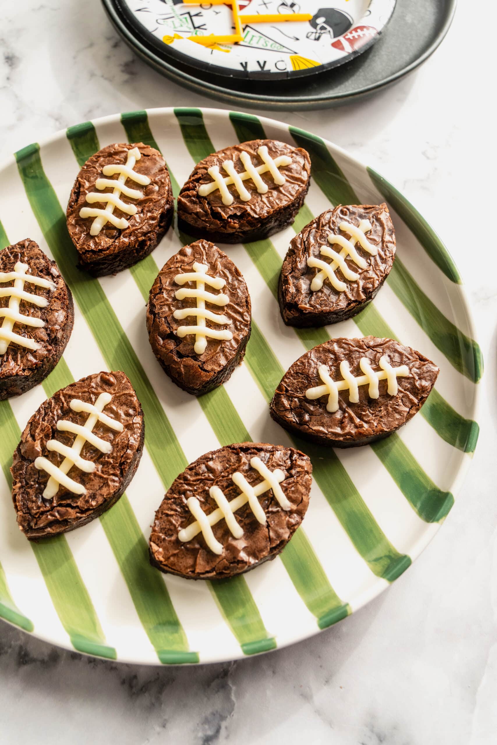 Overhead view of football brownies decorated with white icing laces, arranged on a green striped plate for a fun Super Bowl dessert.