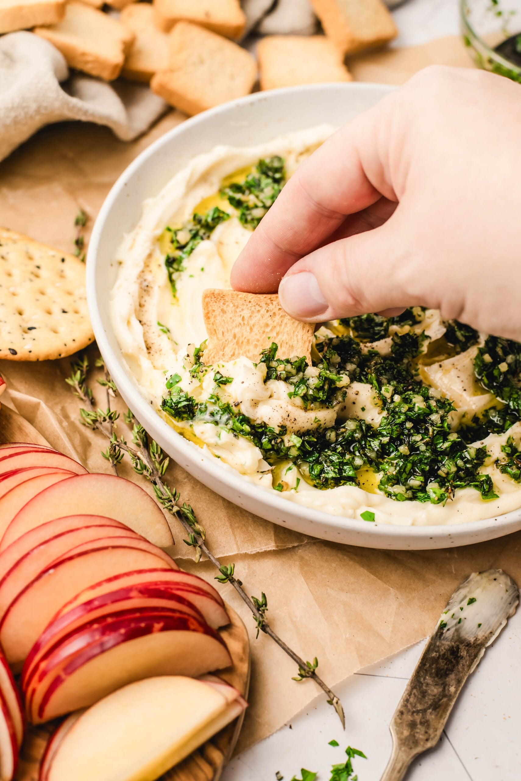 Crostini being dipped into whipped brie topped with garlic herb olive oil, styled close-up with sliced apples, crackers, and fresh thyme around a shallow bowl of creamy whipped brie.
Select 63 more words to run Humanizer.
