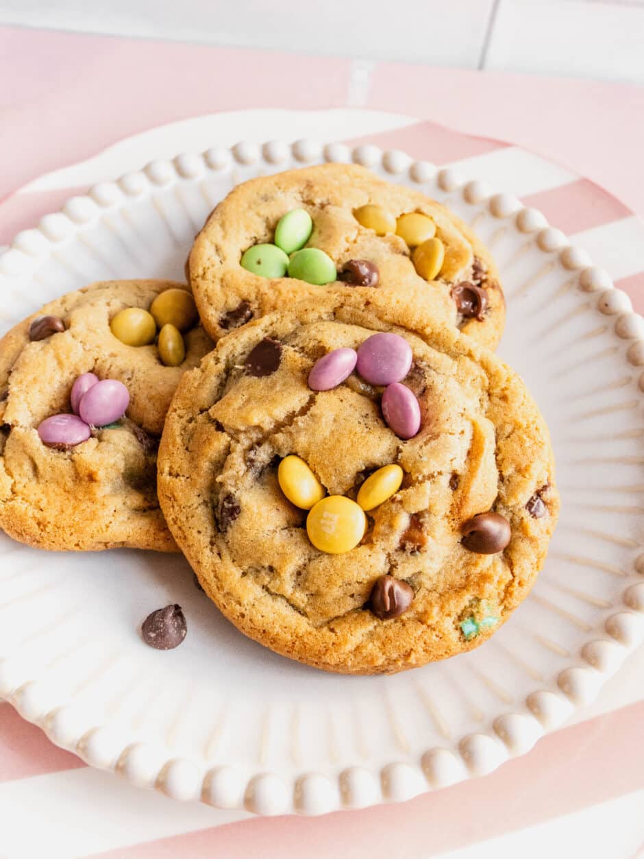 Close-up of soft baked Easter bunny cookies on a white plate, decorated with pastel M&Ms arranged like bunny ears and faces, with chocolate chips throughout.